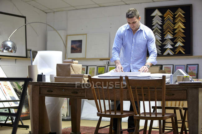 Homem que envolve a imagem no envoltório da bolha na tabela na oficina dos framers da imagem — Fotografia de Stock