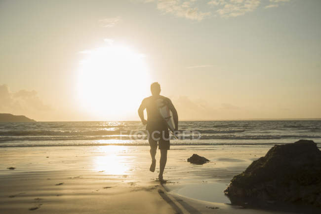Зрелый человек, бежит к морю, держа доску для серфинга — стоковое фото
