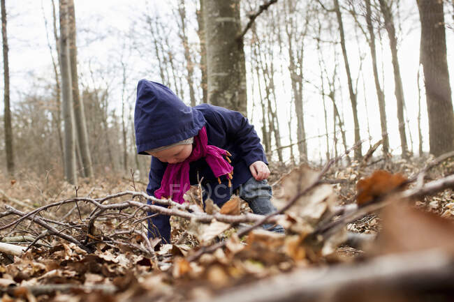 Criança fêmea se curvando para a frente para brincar com folhas de outono — Fotografia de Stock