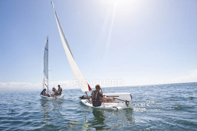 Jóvenes amigos adultos compiten entre sí en veleros en el mar - foto de stock
