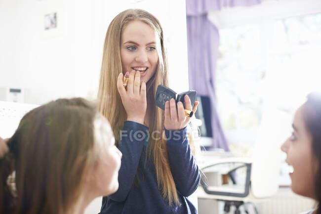 Adolescente chica con amigos aplicando lápiz labial en el dormitorio - foto de stock