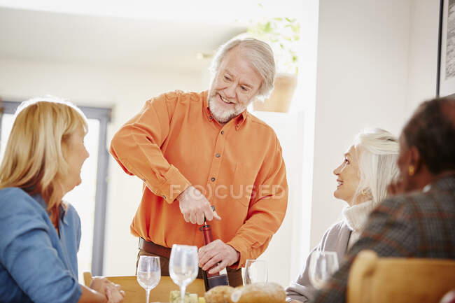 Старший мужчина открывает вино с друзьями — стоковое фото