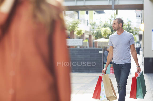 Homem adulto médio segurando sacos de compras, andando atrás da mulher — Fotografia de Stock