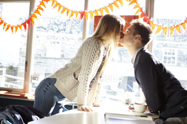 Romántica pareja joven besándose sobre la mesa en la cafetería - foto de stock