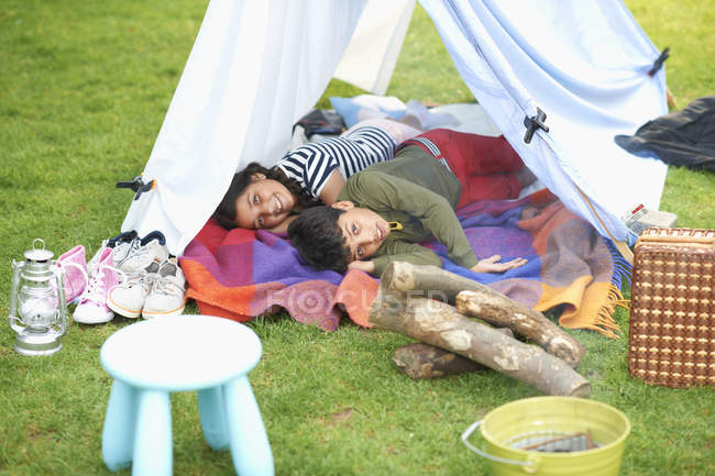 Irmão e irmã deitados em tenda caseira no jardim — Fotografia de Stock
