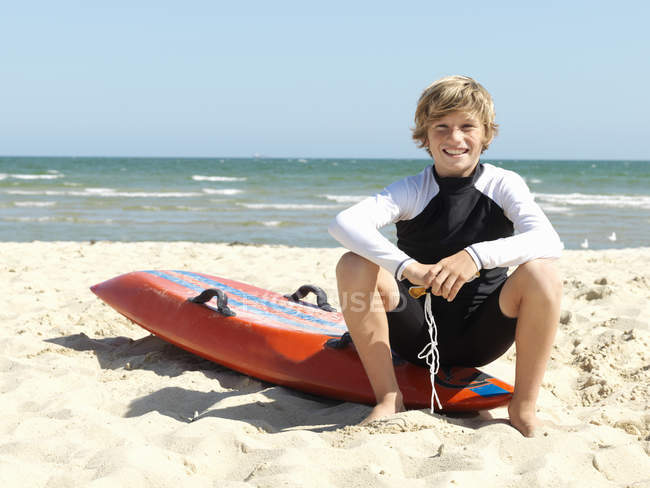 Retrato de un niño confiado (niños salvavidas) sentado en la tabla de surf en la playa, Altona, Melbourne, Australia - foto de stock