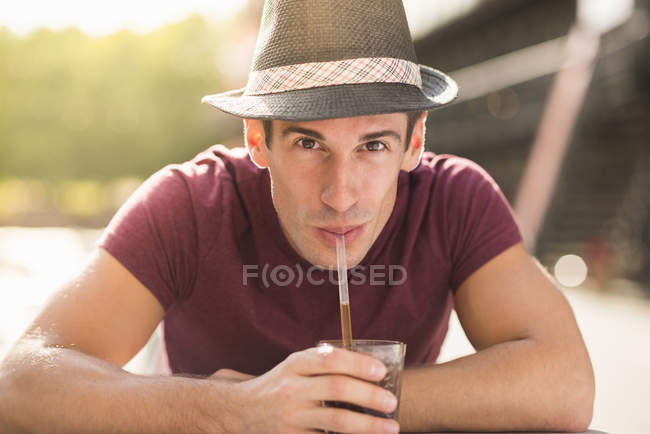 Young man wearing hat drinking through straw — Stock Photo