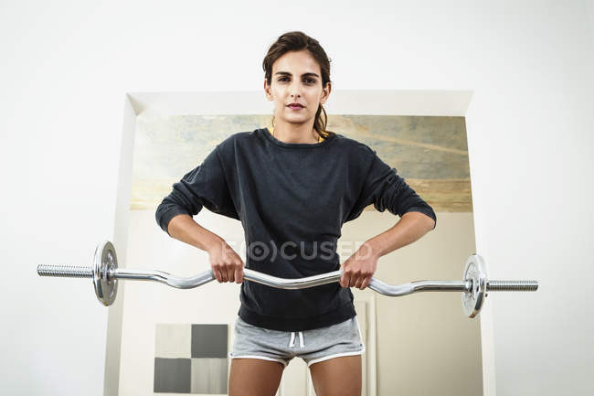 Young woman lifting barbell in living room — Stock Photo