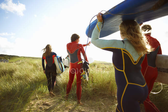 Group of surfers heading towards beach, carrying surfboards, rear view — Stock Photo