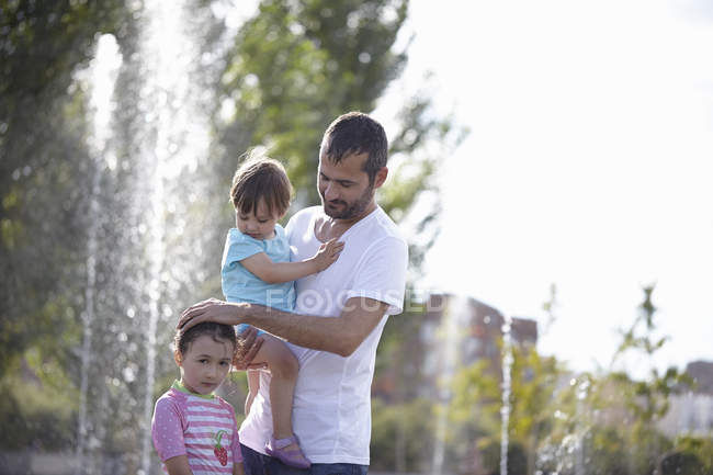 Mid adult man and two daughters standing in water fountains, Madrid, Spain — Stock Photo
