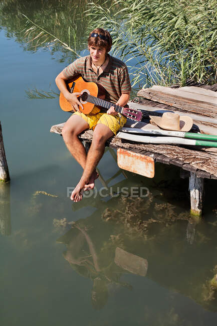 Человек, сидящий на причале и играющий на гитаре — стоковое фото