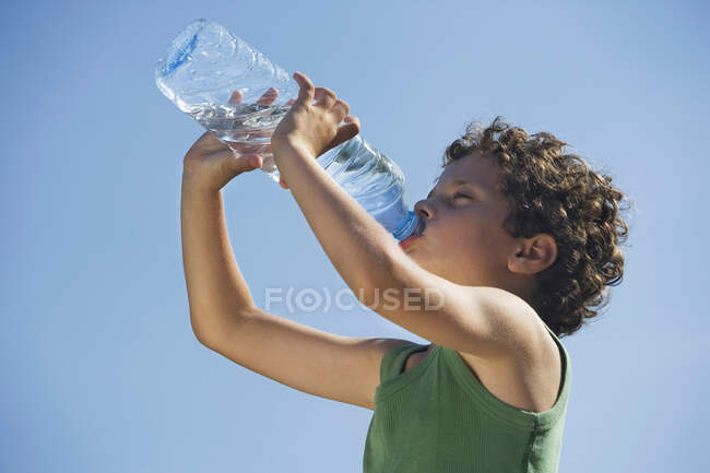 Retrato de niño bebiendo agua de la botella con el cielo al fondo - foto de stock