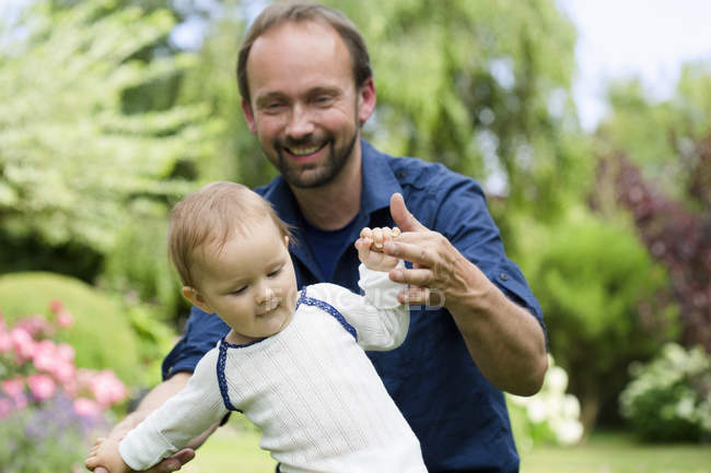 Father holding baby daughter hands whilst toddling — Stock Photo