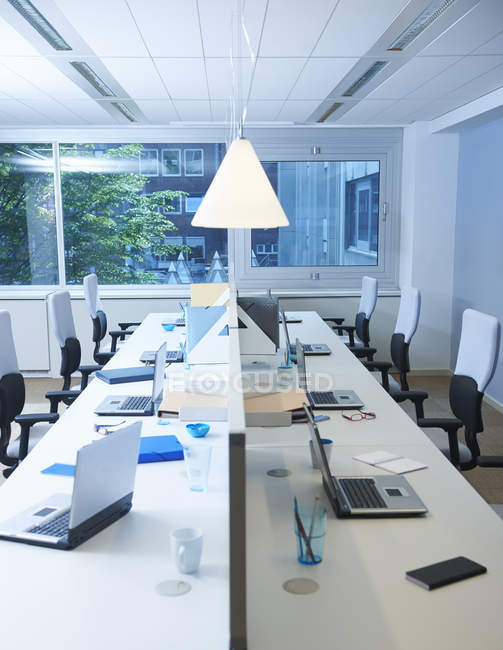 Empty office interior with long table full with laptop computers and illuminating lamp — Stock Photo