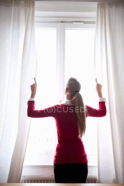 Mujer abriendo cortinas de ventana - foto de stock
