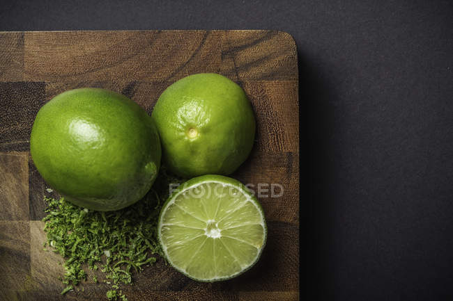 Whole lime with halves and lime peel on wooden board — Stock Photo
