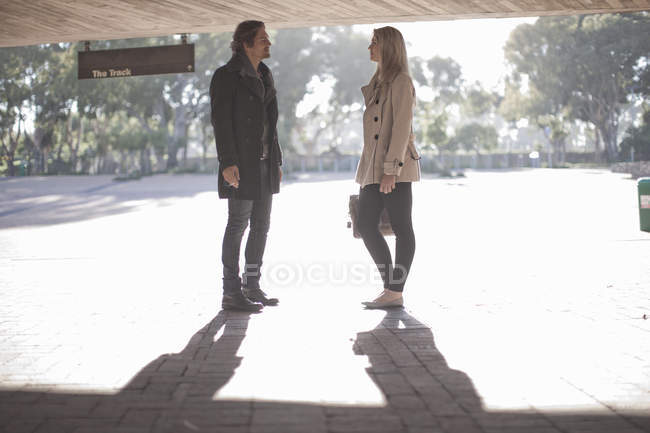 Young woman chatting to mid adult man in city underpass — Stock Photo