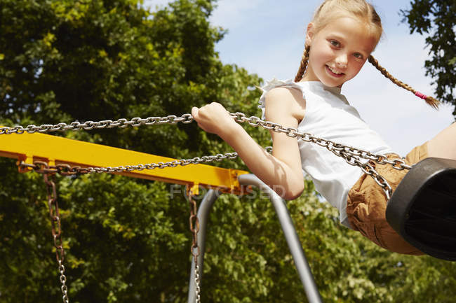 Girl with pigtails on swing looking at camera smiling — Stock Photo
