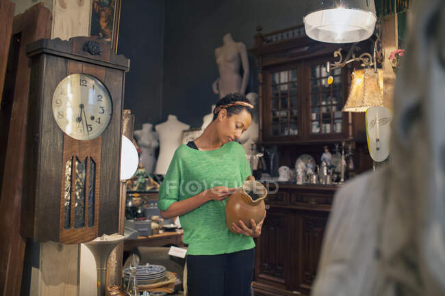 Mujer joven mirando la entrada del precio de la jarra en la tienda vintage - foto de stock