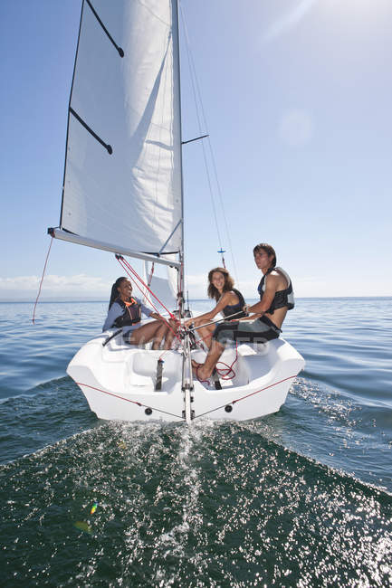 Three young friends relaxing on sailboat on water — Stock Photo