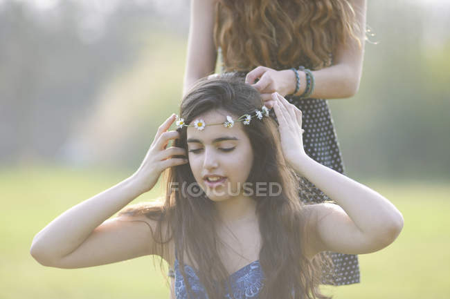 Two teenage girls putting on and wearing daisy chain headdresses in park — Stock Photo