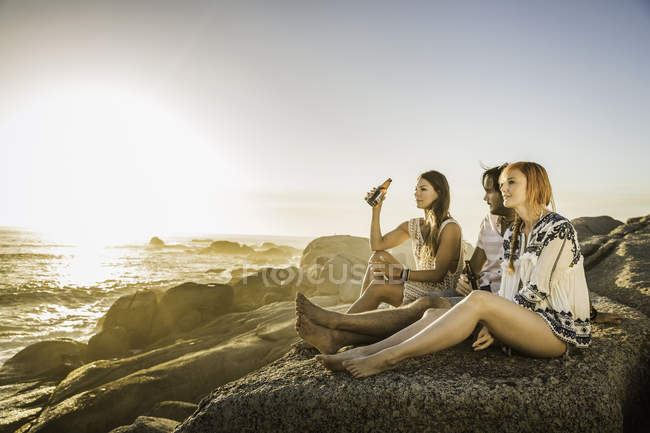 Três adultos médios sentados na praia com vista para o pôr do sol, Cidade do Cabo, África do Sul — Fotografia de Stock