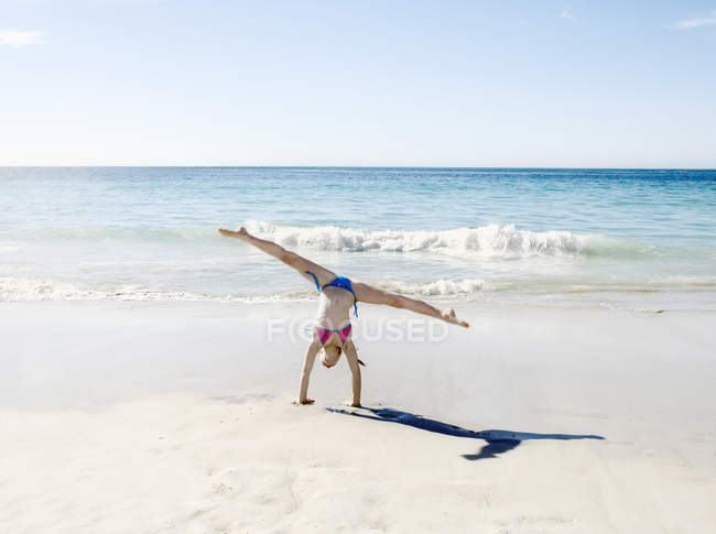 Девушка делает стойку на руках и расщепляется на пляже — стоковое фото
