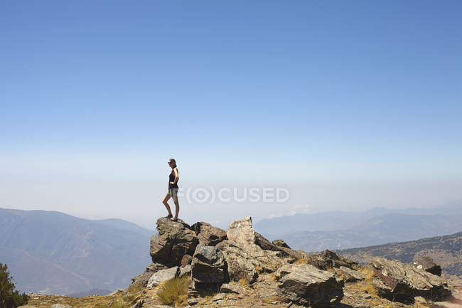 Young woman standing on top of rocks gazing at view, Sierra Nevada, Andalucia Granada, Spain — Stock Photo