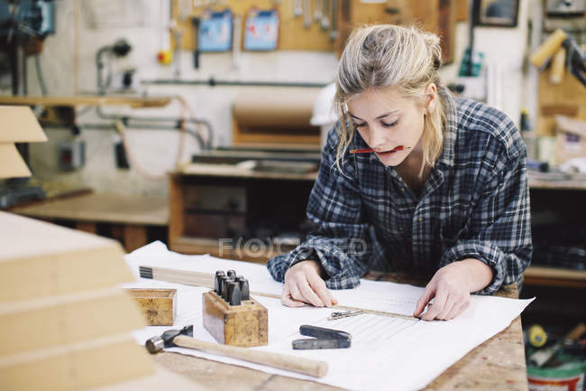 Young craftswoman measuring blueprint on workbench in pipe organ workshop — Stock Photo