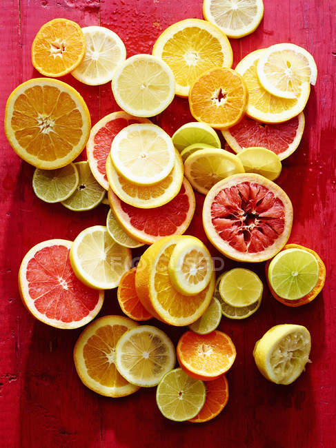 Zitrusfruchtscheiben auf roter, rustikaler Oberfläche — Stockfoto