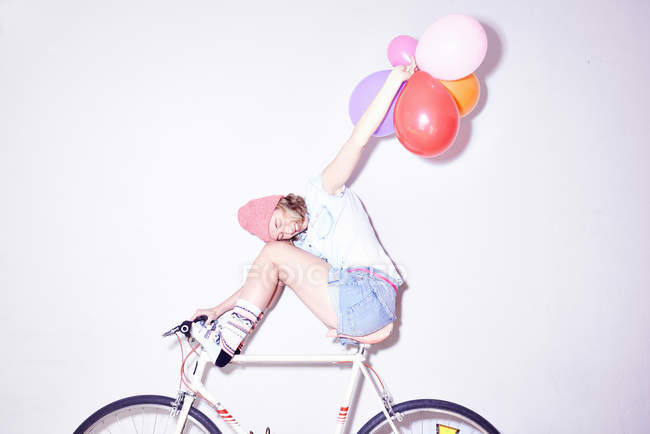 Young woman sitting on bicycle and holding bunch of balloons — Stock Photo