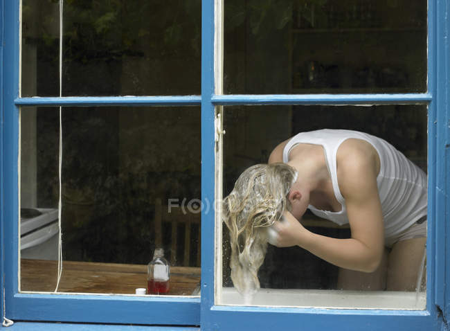 Vista da janela da jovem mulher lavando o cabelo na bacia — Fotografia de Stock