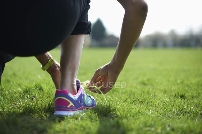 Cropped rear view of mature woman tying trainer laces in park — Stock Photo