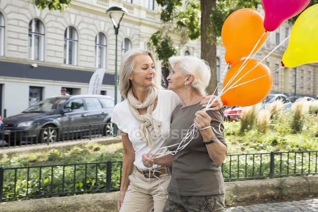 Mãe e filha andando juntos na rua, segurando um monte de balões — Fotografia de Stock