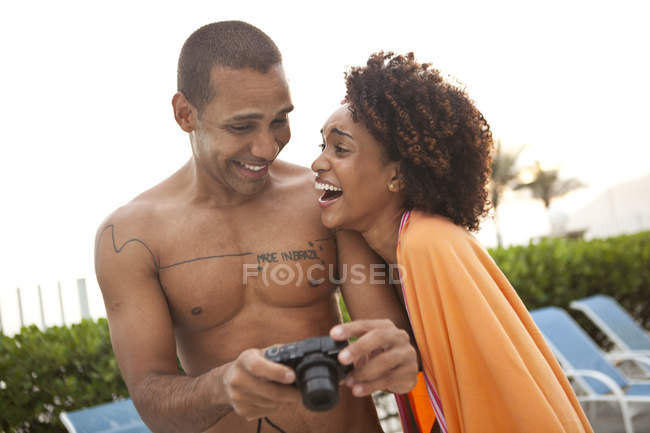 Paar lacht über Fotos auf Digitalkamera am Hotelpool, Rio de Janeiro, Brasilien — Stockfoto