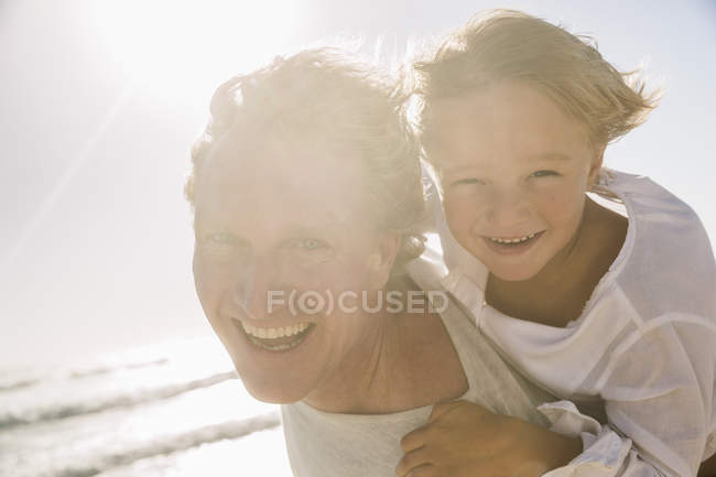 Père sur la plage donnant fils piggy retour en regardant la caméra souriant — Photo de stock