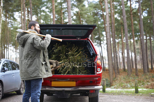 Jovem com machado e árvore de Natal picada na bota do carro — Fotografia de Stock