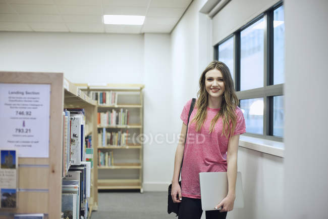 Молода жінка тримає ноутбук у бібліотеці — стокове фото