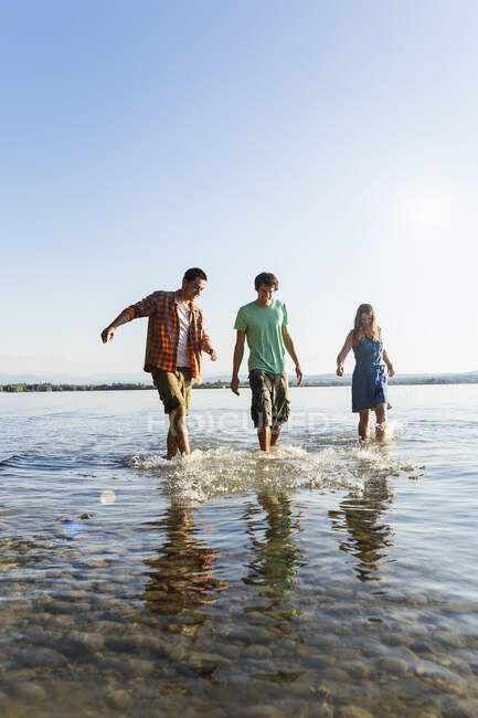 Front view of friends in a row walking ankle deep in water, Schondorf, Ammersee, Bavaria, Germany — Stock Photo