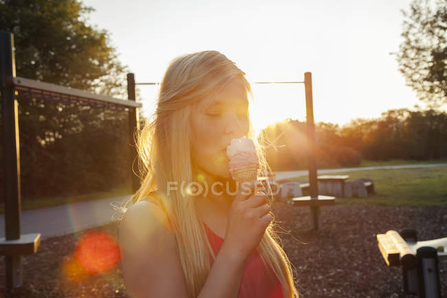 Young woman eating ice cream cone in park at sunset — Stock Photo