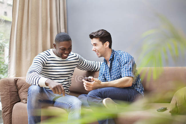 Два молодых человека со смартфоном на диване в гостиной — стоковое фото