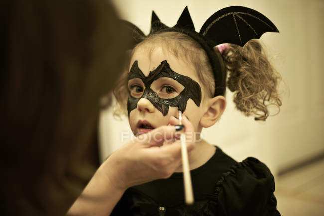 Mother painting daughter face for Halloween bat costume — Stock Photo