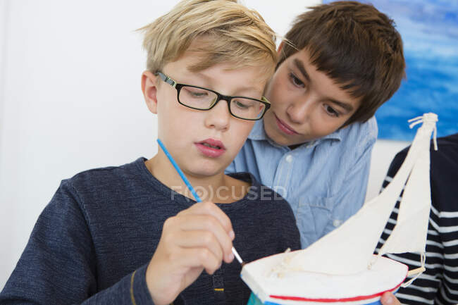 Teenage boy and brother painting toy boat at kitchen table — Stock Photo