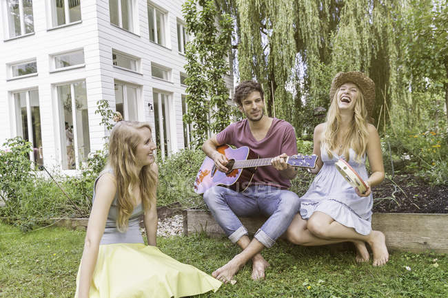 Three friends in garden, man playing guitar — Stock Photo