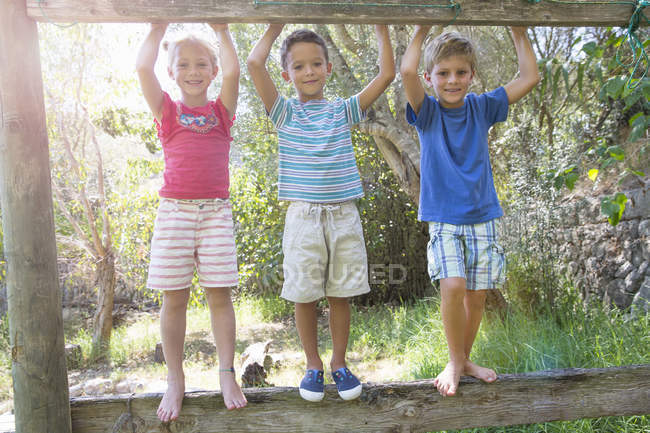 Portrait of three children standing on fence in garden — Stock Photo