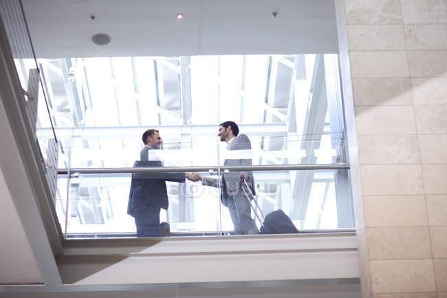 Dos jóvenes empresarios estrechando la mano en el balcón del centro de conferencias - foto de stock