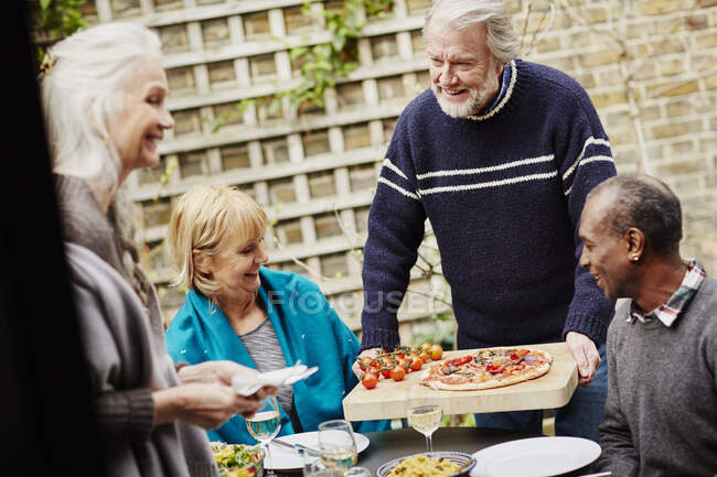 Старший мужчина подает друзьям пиццу в саду — стоковое фото