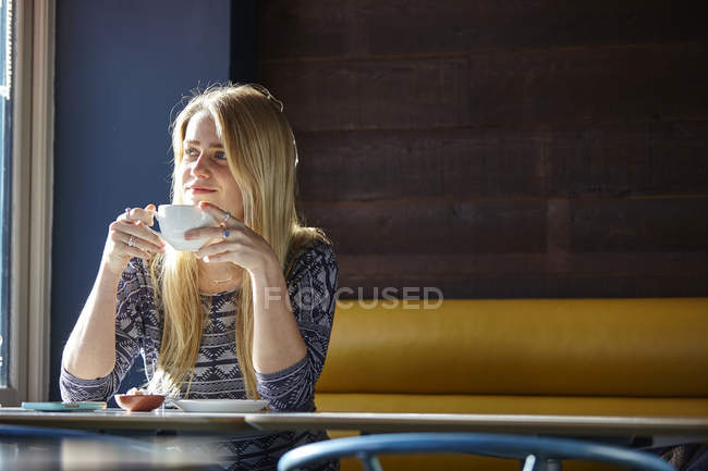 Jeune femme seule au café boire du café — Photo de stock