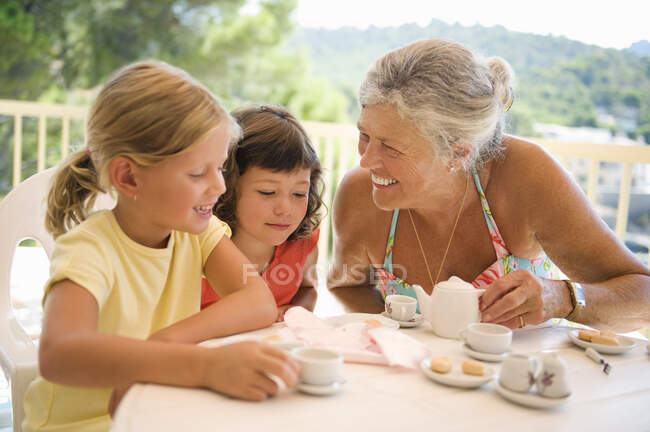 Una mujer mayor y niños tomando té - foto de stock