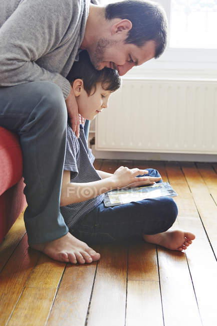 Батько і син використовують цифровий планшет на дерев'яній підлозі — стокове фото